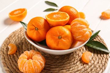 Bowl with sweet mandarins and leaves on white wooden background, closeup