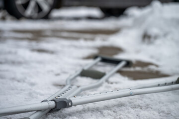 Crutches rest on snowy ground outside a car during winter weather in the late afternoon