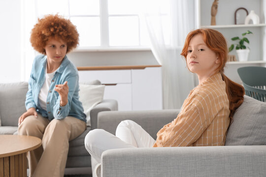 Redhead mother squabbling with her teenage daughter on sofa at home
