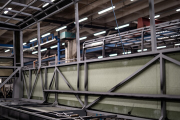 Naklejka premium Industrial vehicle manufacturing workshop with metal bus frames and body structures under assembly. Large factory interior shows fabrication, welding, and custom vehicle production in progress.