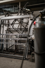 Industrial vehicle manufacturing workshop with metal bus frames and body structures under assembly. Large factory interior shows fabrication, welding, and custom vehicle production in progress.