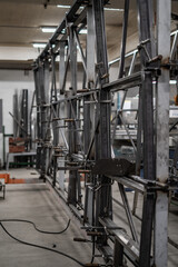 Industrial vehicle manufacturing workshop with metal bus frames and body structures under assembly. Large factory interior shows fabrication, welding, and custom vehicle production in progress.