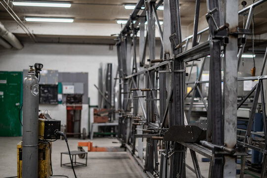 Industrial vehicle manufacturing workshop with metal bus frames and body structures under assembly. Large factory interior shows fabrication, welding, and custom vehicle production in progress.