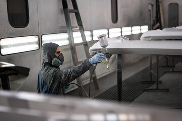 Fototapeta premium Worker spray painting vehicle body part in professional paint booth. Industrial automotive painting process with protective equipment, precision tools, and controlled environment.