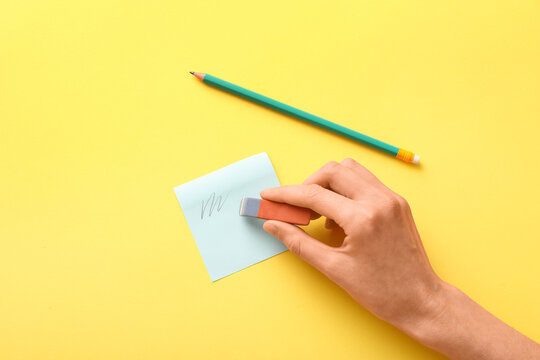 Female hand with eraser, sticker and pencil on yellow background