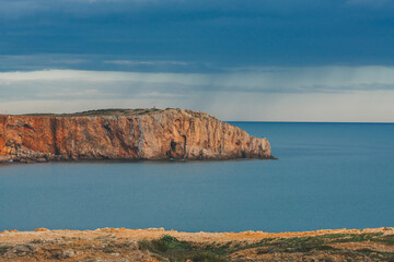 Dramatic cliffs meet calm blue waters as storm clouds gather in the distance.