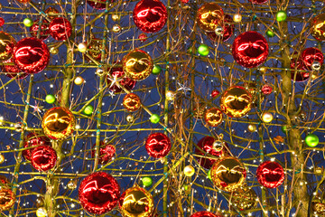 Fototapeta premium Colorful Christmas baubles ornaments in red gold green on festive tree branches with lights