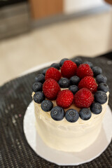 A small cake decorated with white icing, strawberries and blueberries