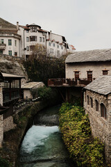 Narrow river canal flowing through the old town of Mostar between stone houses and wooden terraces. Quiet historic city scene showing traditional Balkan architecture and everyday atmosphere.