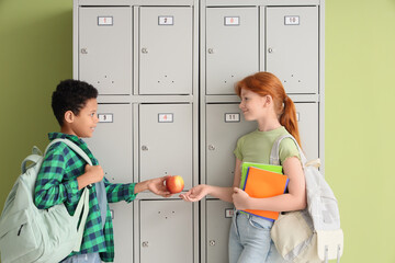 Teenage students with apple and copybooks near locker on green background