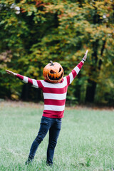 Person Wearing a Pumpkin Head Standing Outdoors in Autumn