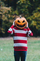 Person Wearing a Pumpkin Head Standing Outdoors in Autumn