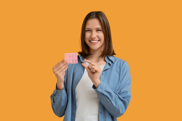 Beautiful young woman holding container with pills on yellow background