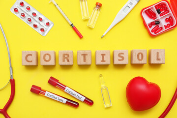 Word CORTISOL with thermometer, blood samples, pills and ampules on yellow background. Medical concept