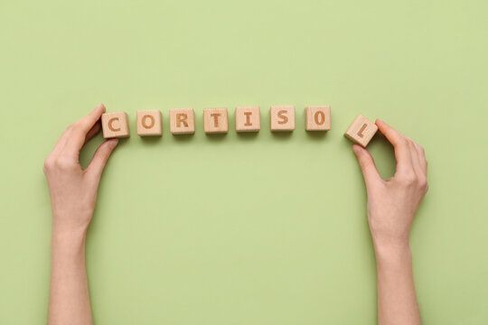 Female hands with word CORTISOL made of wooden cubes on green background. Medical concept