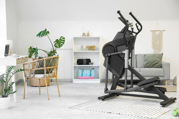 Interior of stylish room with modern exercising bike, workspace, sofa and sports equipment