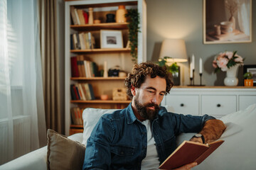 Fototapeta premium Man enjoying reading book relaxing on sofa at home