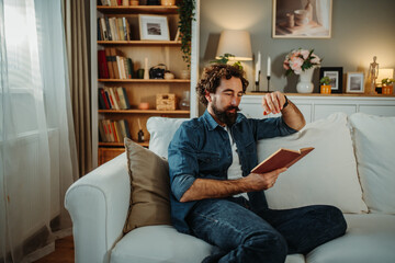 Man relaxing at home reading book on sofa enjoying leisure time