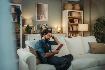 Obraz premium Man relaxing at home reading a book on sofa