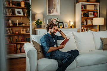 Happy man relaxing on sofa reading book at home