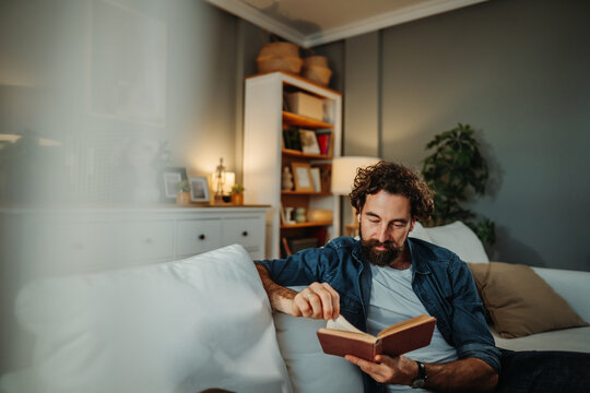 Man relaxing on sofa reading book at home