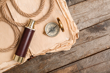 Golden compass, spyglass, old book and rope on wooden background