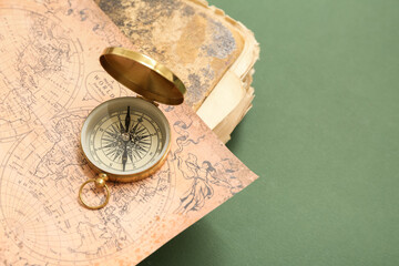 Golden compass, old book and map on green background, closeup