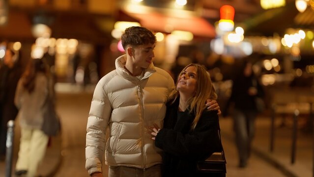 A romantic couple is walking together in Paris France at night with city lights and an urban street background The image conveys love and affection in a European setting.