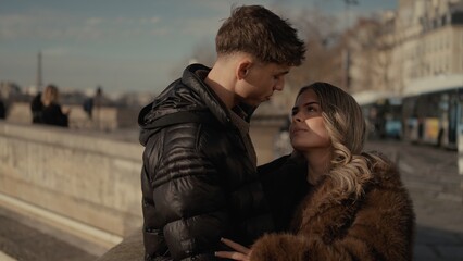 A romantic young couple in love is embracing in Paris France with a cityscape background They are wearing winter coats and looking at each other with affection and tenderness capturing a moment of lov