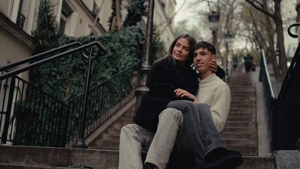 A romantic couple is sitting on the stairs in Montmartre Paris France embracing and enjoying the city view. This image can be used for travel lifestyle or relationship content.