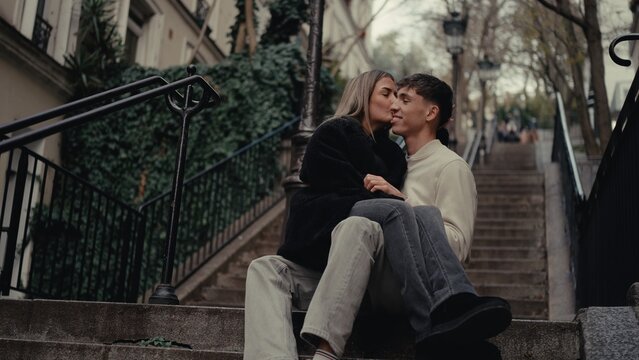 A romantic couple is kissing on stone steps in Montmartre Paris France. This image captures love and affection in an urban cityscape suitable for travel and tourism related content.