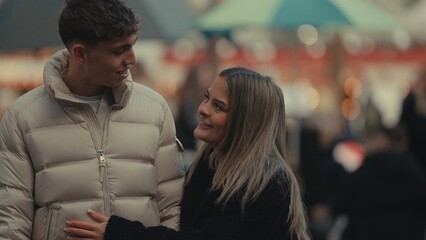 A young couple in Paris France smile at each other while wearing winter coats in an urban setting with bokeh lights in the background. This image is perfect for travel romance and lifestyle concepts.