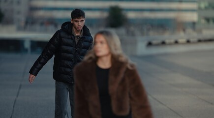 A young couple walks in Paris France with modern architecture in the background The man wears a black puffer jacket and the woman wears a brown fur coat showcasing urban fashion and lifestyle.