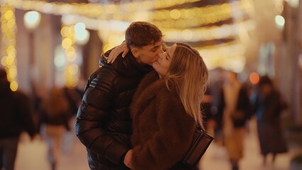 A romantic couple kisses in Paris France at night surrounded by bokeh lights. This image can be used for Valentine's Day promotions travel advertisements or relationship-themed contentment.