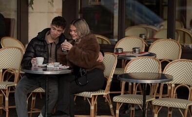 A romantic couple is enjoying coffee at an outdoor in Paris France They are wearing winter coats and embracing showing love and affection in an urban setting.