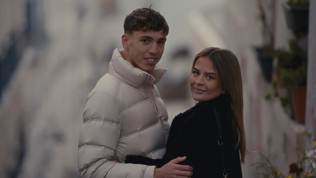 A young couple poses together on a street in Paris France The man wears a beige puffer jacket and the woman wears a black coat creating a stylish and romantic image suitable for fashion and lifestyle 