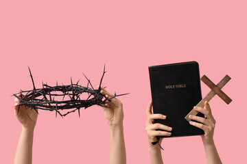 Female hands with crown of thorns, Holy Bible and wooden cross on pink background, closeup. Good Friday concept