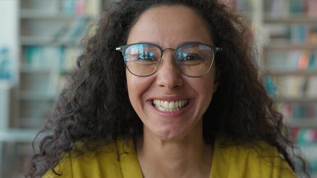 Close up Latino Arabian happy woman smiling at camera in library female girl student with glasses enjoying reading bookshelf bookstore university intelligent pleasure laughter bookworm reader learning