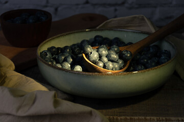 Wooden spoon with blueberries illuminated by a ray of sunlight in a bowl.