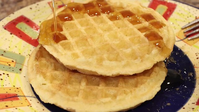 drizzling maple syrup over a stack of waffles