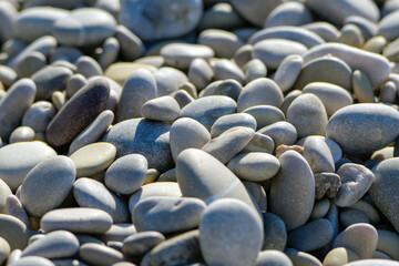 A close up of smooth light and dark gray stones and rounded pebbles forming a natural pattern on the beach ground under bright sunlight © Buğra Kaan Ersoy
