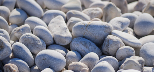 Fototapeta premium A close up view of light gray white rounded pebbles and stones covering a natural Mediterranean beach on a sunny day perfect for a summer holiday background