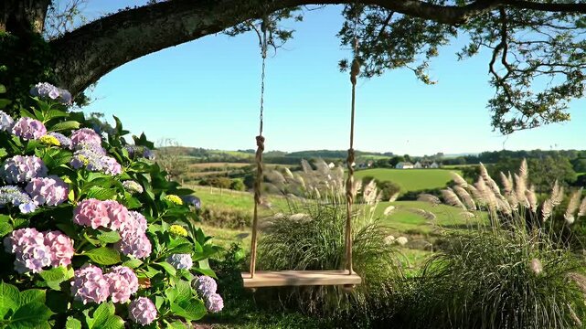 Tranquil countryside garden scene featuring a hanging wooden swing beside pink hydrangea and ornamental grasses under a clear blue sky