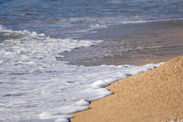 Sea water receding from the sandy shore leaving behind a smooth wet surface and white foam lines under the warm sun