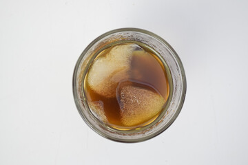 Top view of a refreshing glass of iced coffee with melting ice cubes on white background