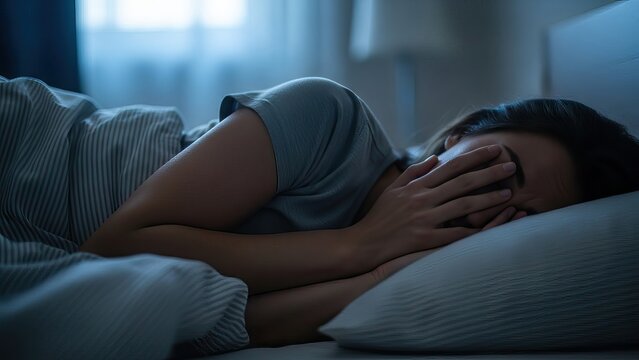 A woman lies asleep in bed, covered in a blanket with her hands over her face. Fighting depression.