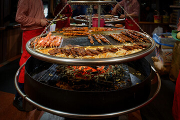 Large round swivel grill with sizzling pork steaks, skewers and onions over glowing coals at a festive Christmas market in Cologne, Germany