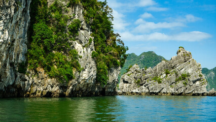 Close-up of steep, moss-covered limestone cliffs rising directly from the emerald green water of Ha Long Bay