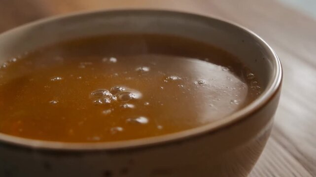 A close up ceramic bowl filled with golden-brown broth, surface bubbles visible suggesting recent heat or stirring in minimal food macro scene