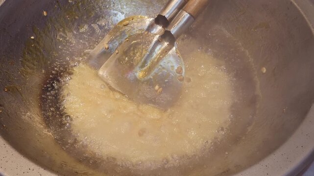 Close up view of boiling malt sugar in iron pan with two spatulas, 4k slow motion footage, Chinese traditional food concept.